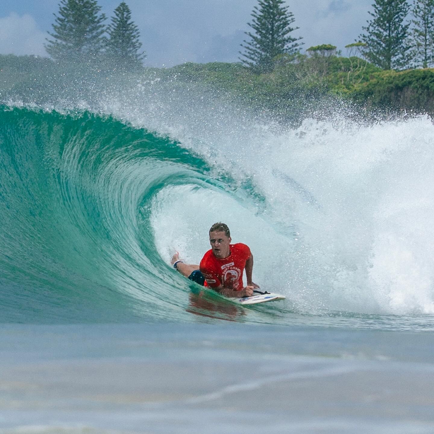 Kai Colless surfing prone in the barrel of a wave at a competition