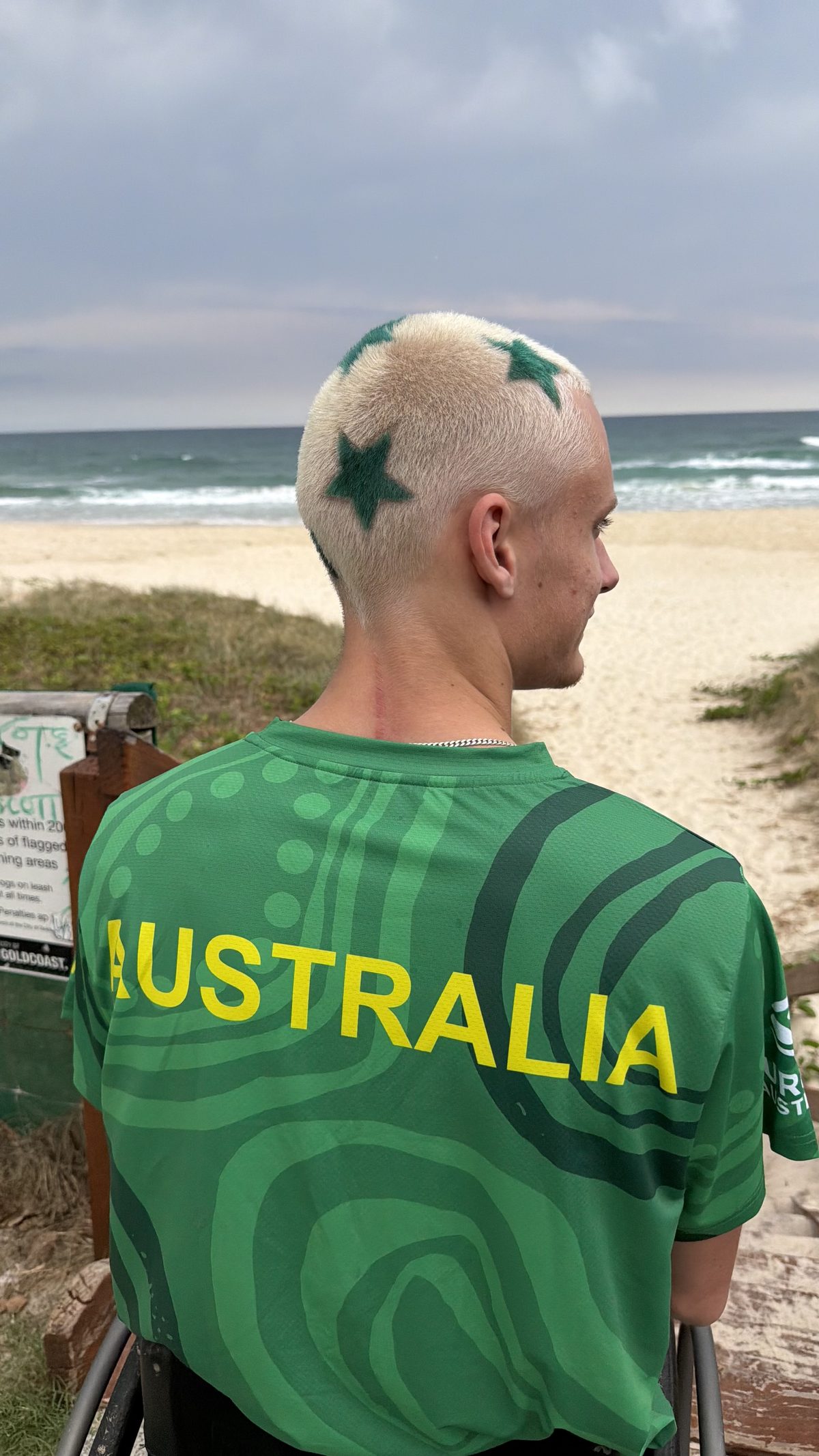 Kai Colless wearing the Australian Irukandjis team jersey at the beach, with green stars dyed into his hair