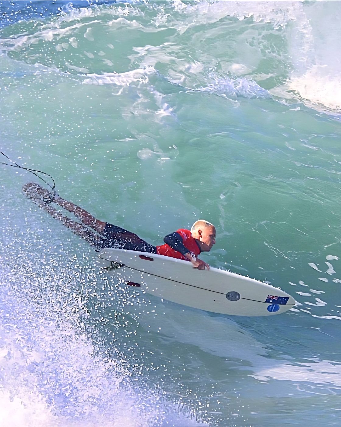 Kai Colless prone surfing a wave on a board with the Australian flag