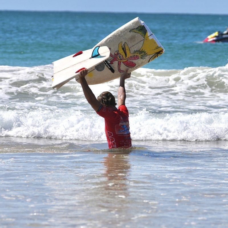 Kai holding his surfboard above his head in the shorebreak after a heat